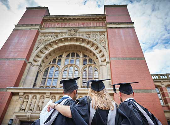 graduates in cap and gown in front of red brick building